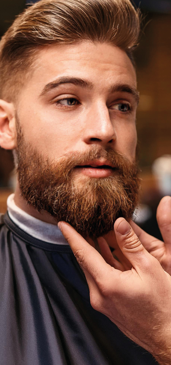 Volto di un uomo con barba lunga e delle mani di un barbiere che applica l'olio alla barba